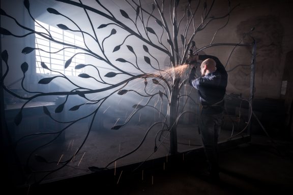 Rankgerüst Mann interagiert mit einer großen, filigranen Metallbaumstruktur in einem nebligen Raum.