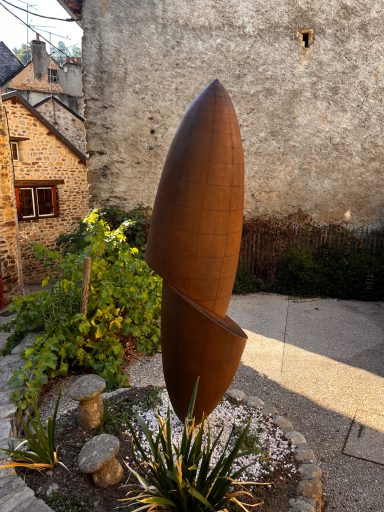 Abstrakte Metallskulptur Abstrakte Skulptur aus Metall, auf einem Pflastersteinboden vor einer historischen Wand.